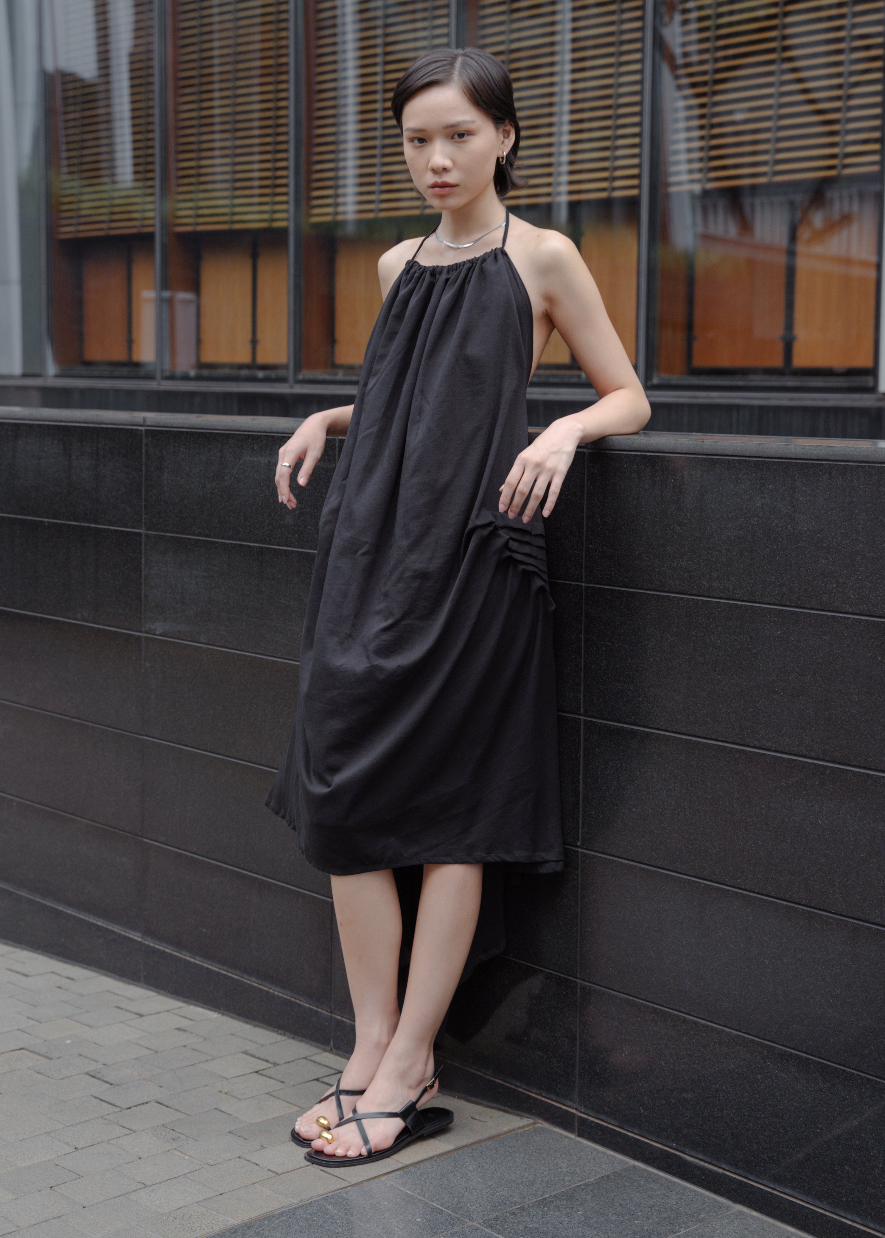 Woman in a black dress standing against a modern building.