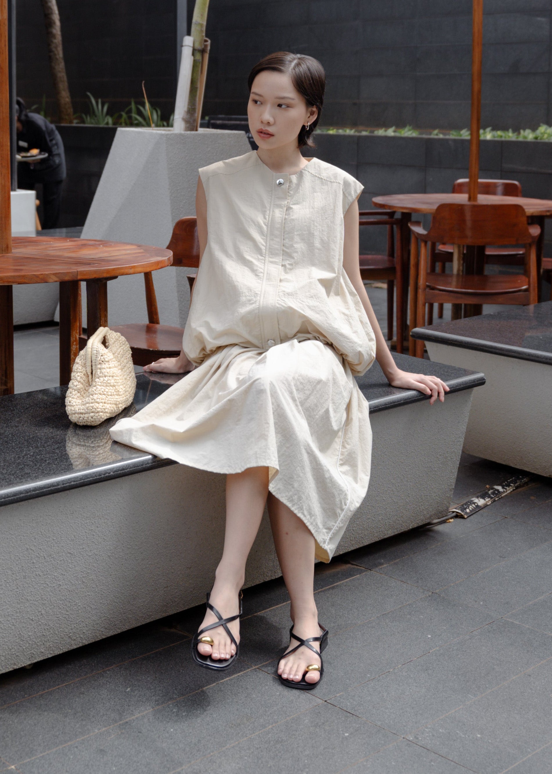 Woman in a white dress sitting on a rooftop with outdoor furniture and umbrellas.
