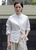 Woman wearing a white blouse and beige pants standing against a black and gray wall.