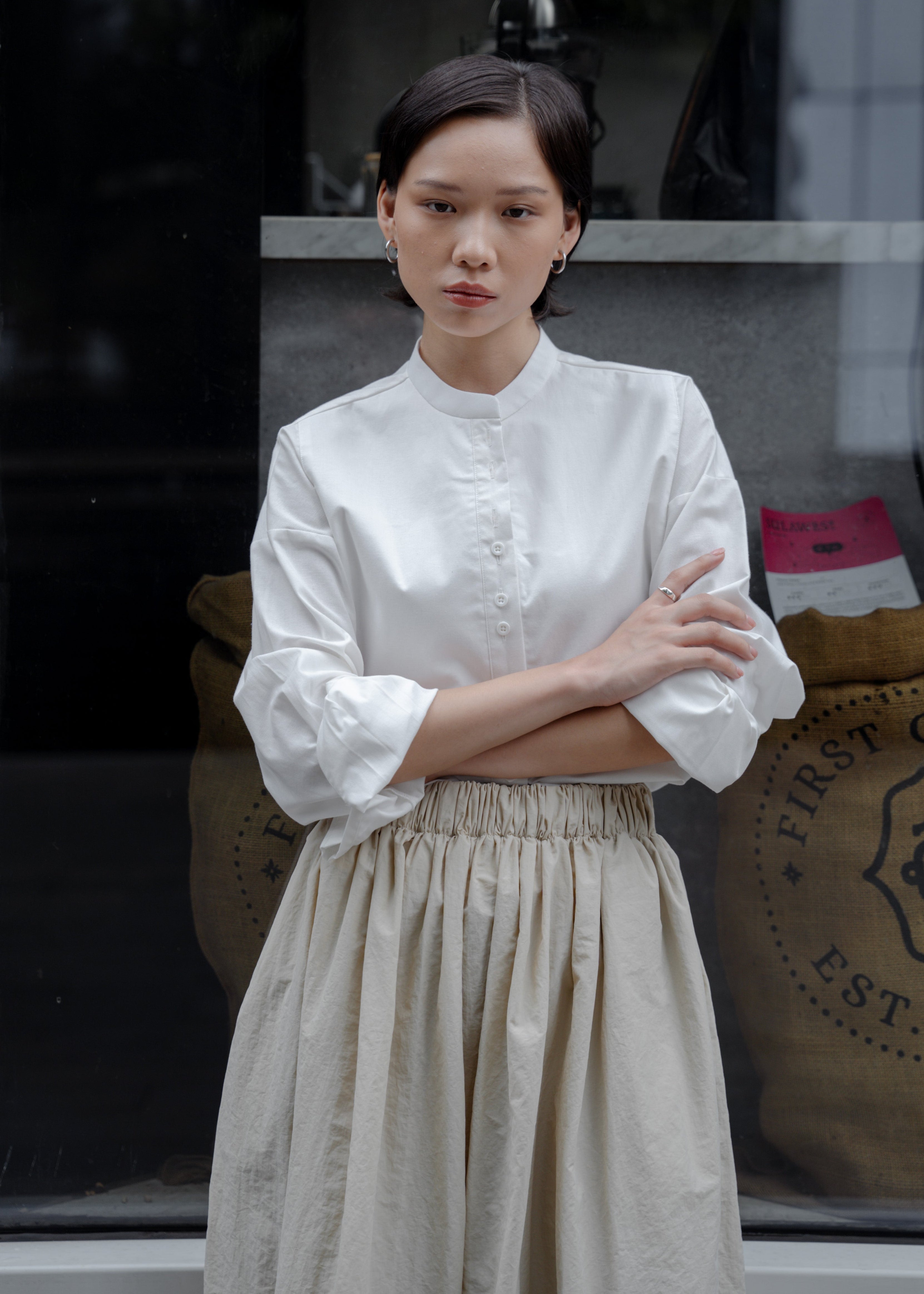 Woman in a white blouse and beige skirt standing in front of a store window.