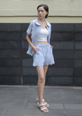Woman wearing a light blue outfit standing against a dark stone wall.