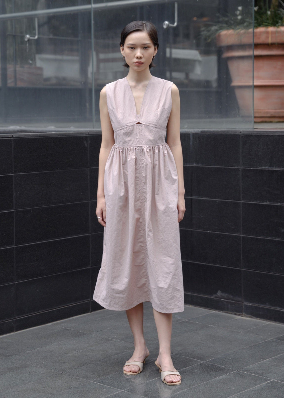 Woman wearing a light pink sleeveless dress standing against a black tiled wall.