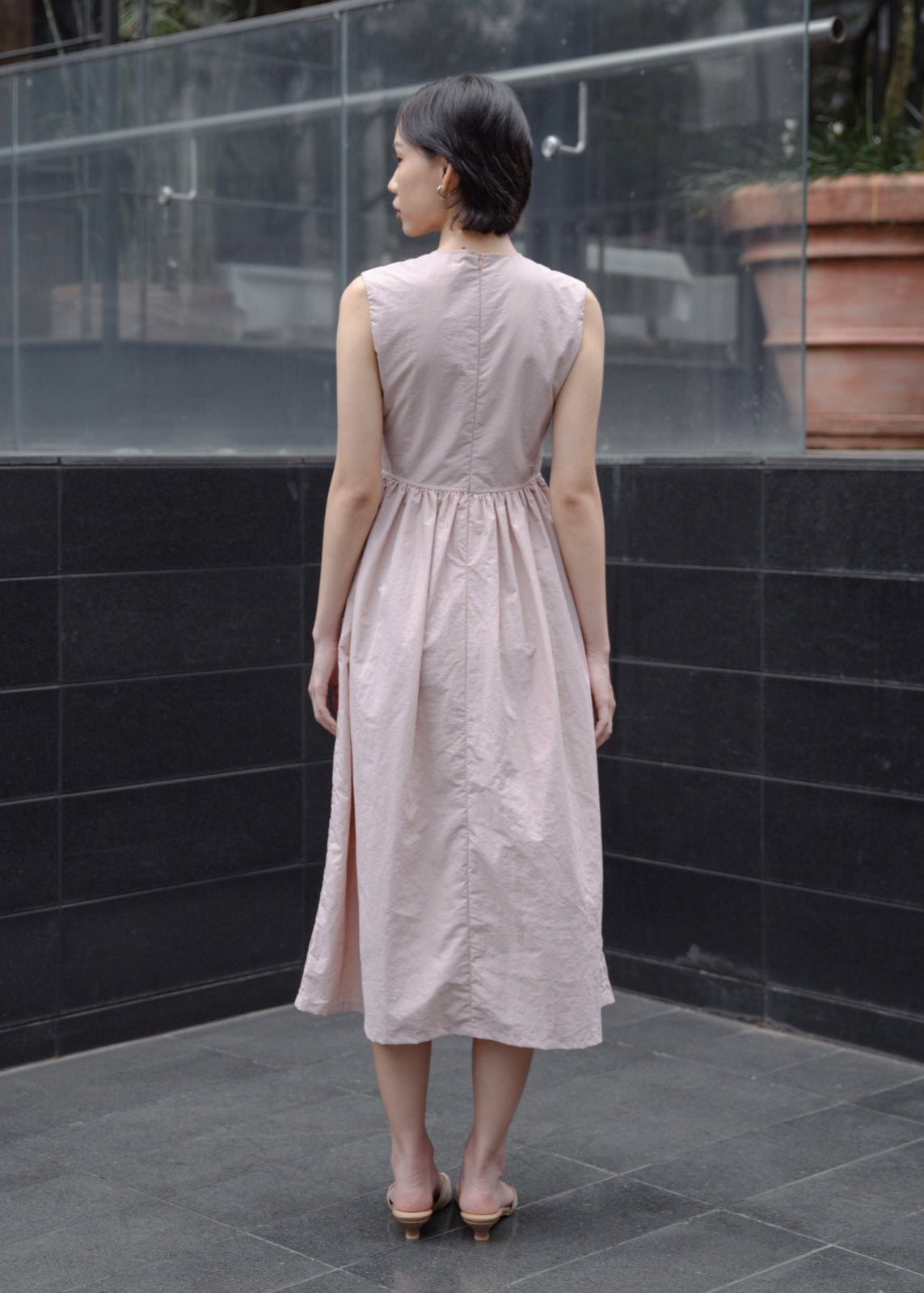 Woman in a light pink dress standing in front of a black tiled wall.