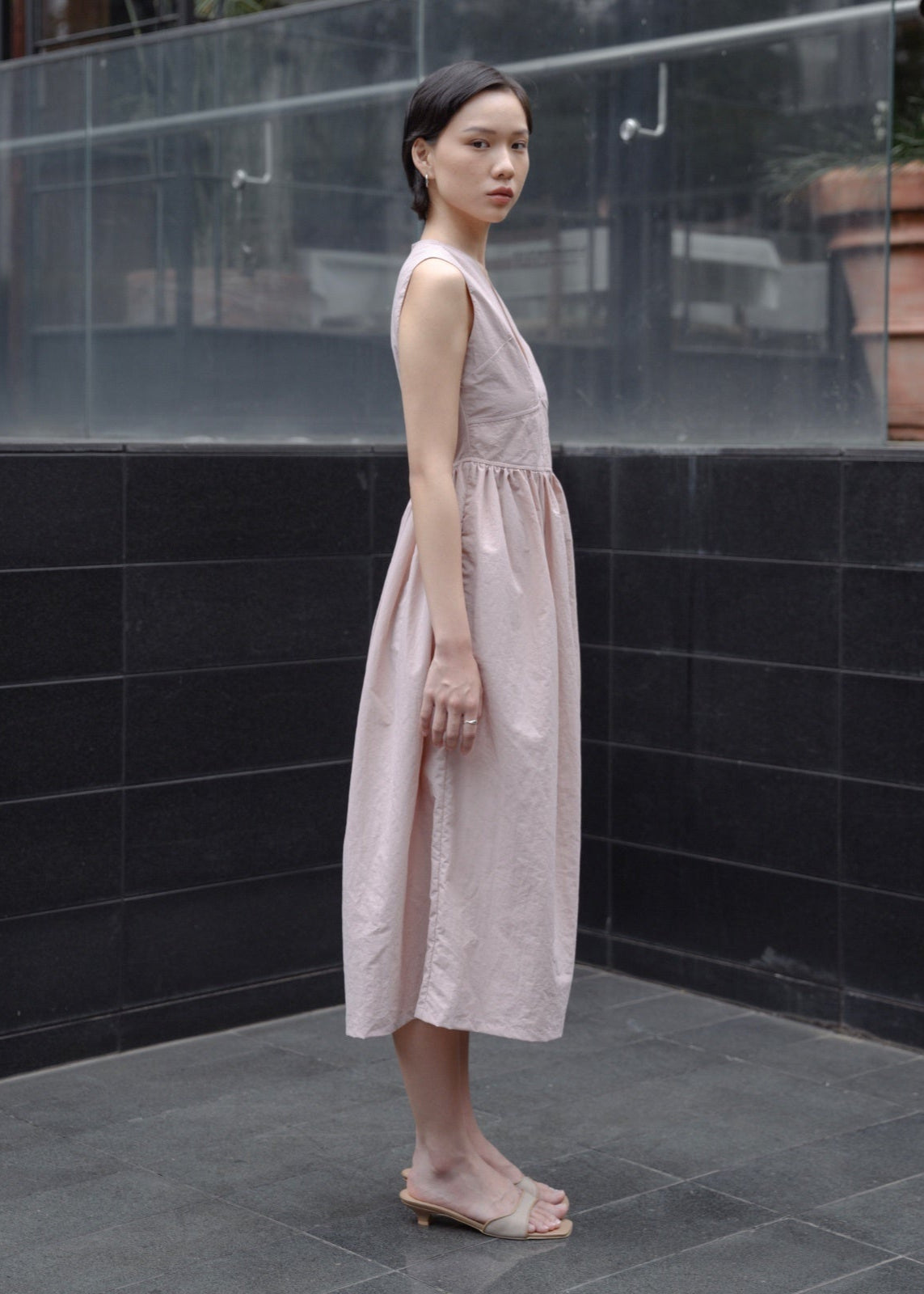 Woman in a light pink dress standing against a black tiled wall.