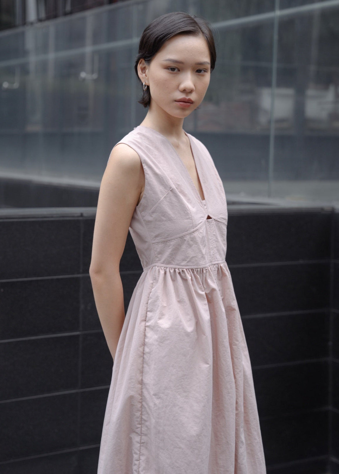 Woman wearing a light pink dress standing against a black wall.