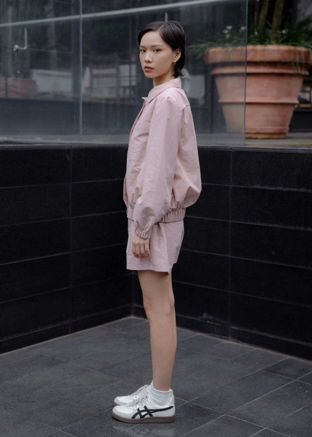 Woman in a pink outfit standing in front of a black tiled wall.