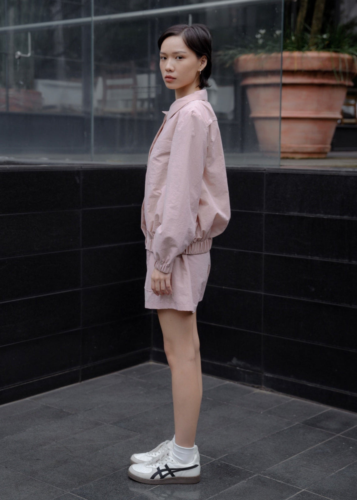 Woman in a pink outfit standing in front of a black tiled wall.