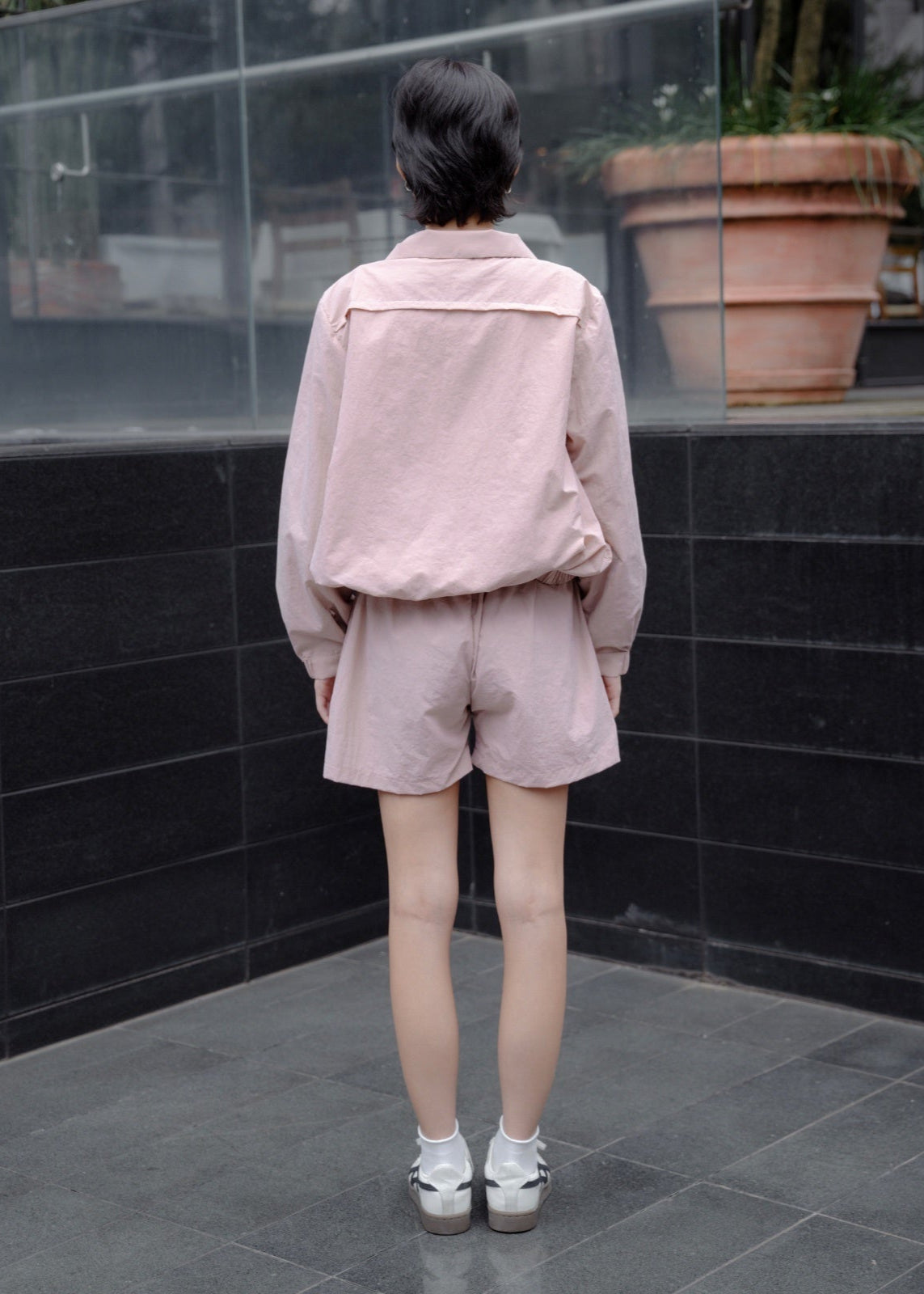 Person wearing a pink outfit standing in front of a black tiled wall.