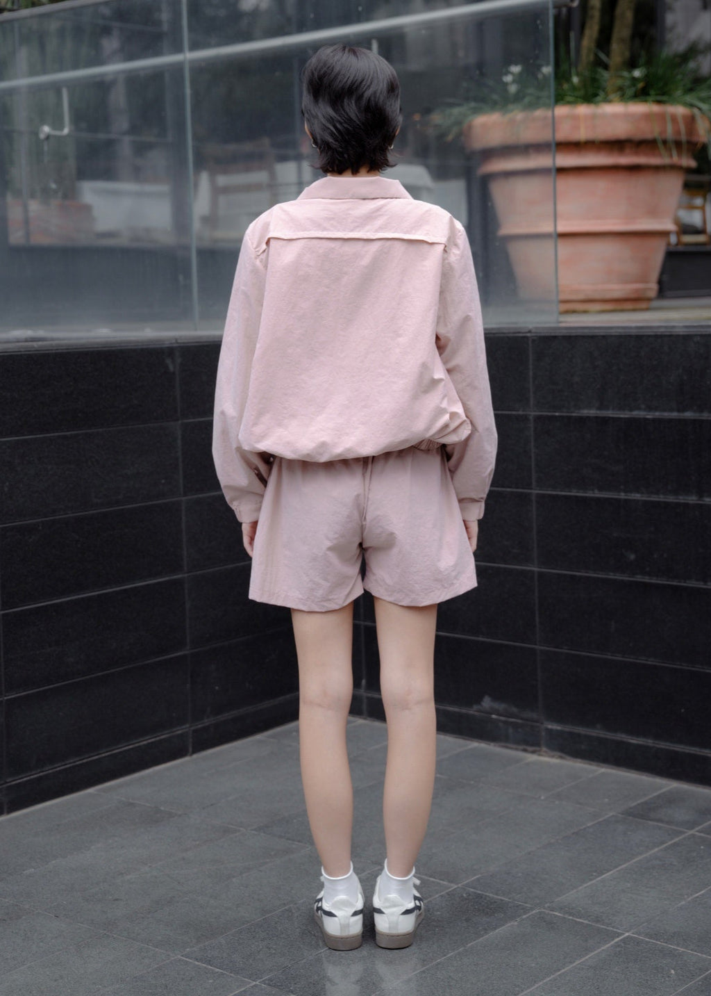 Person wearing a pink outfit standing in front of a black tiled wall.