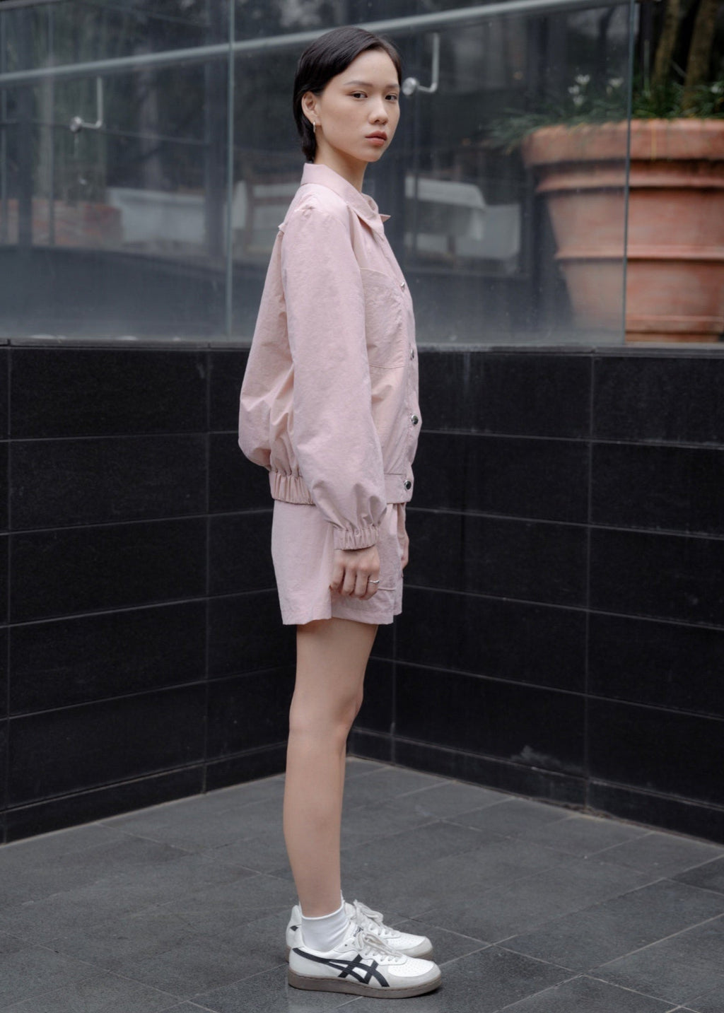 Person wearing a light pink outfit standing against a black tiled wall.