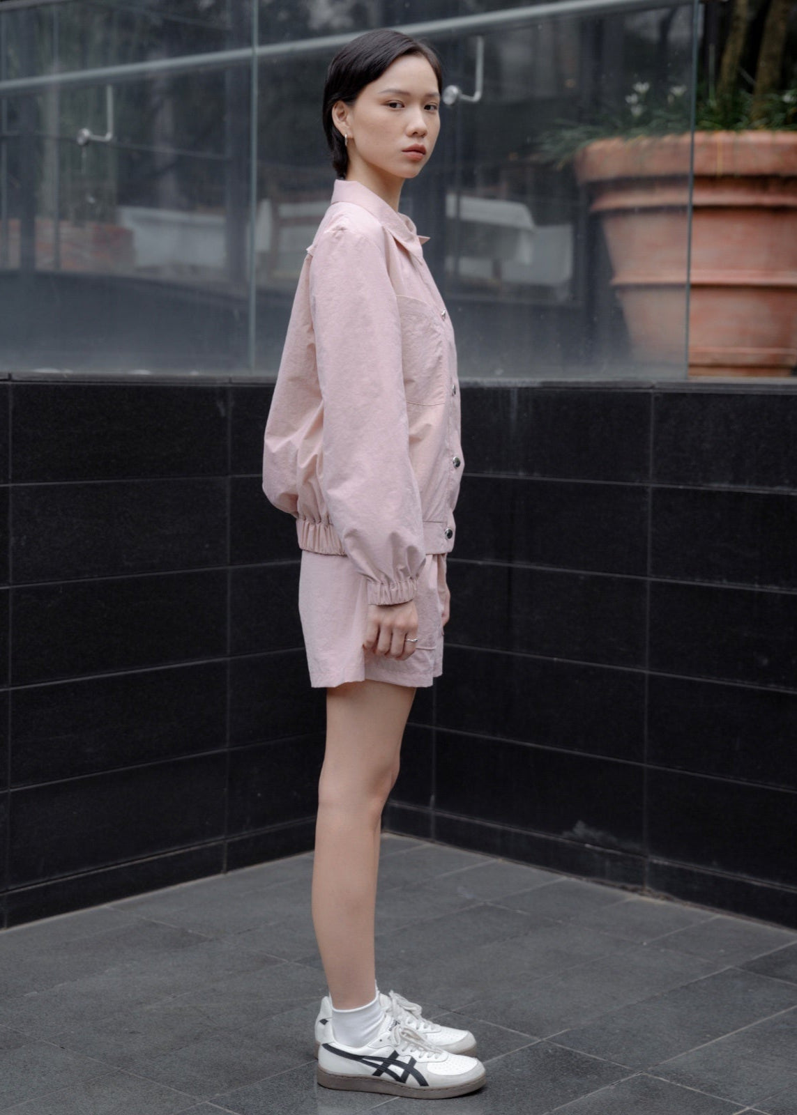 Person wearing a light pink outfit standing against a black tiled wall.