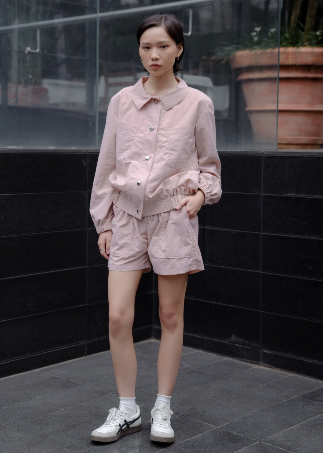 Person wearing a pink outfit standing against a black tiled wall.