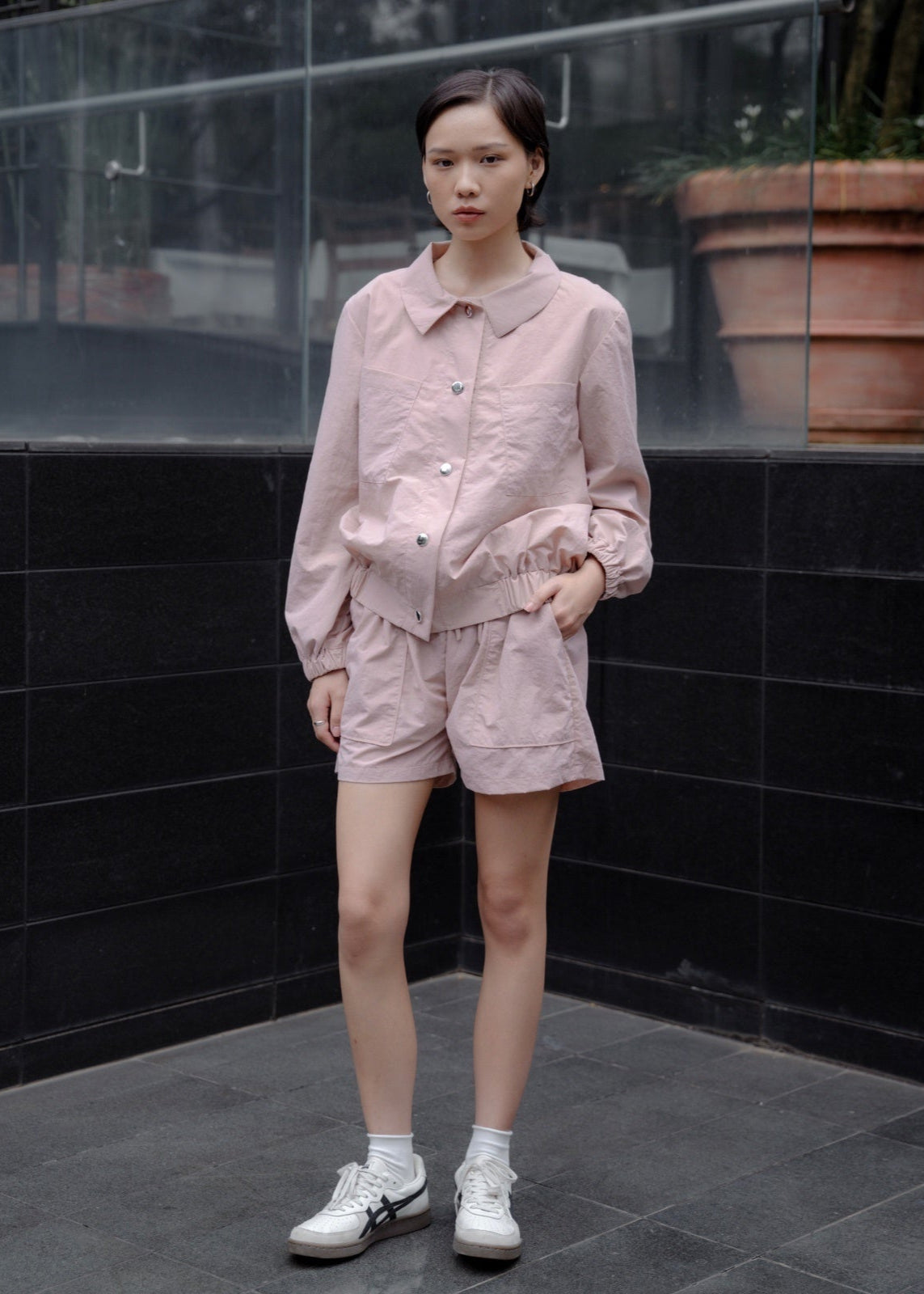 Person wearing a pink outfit standing against a black tiled wall.