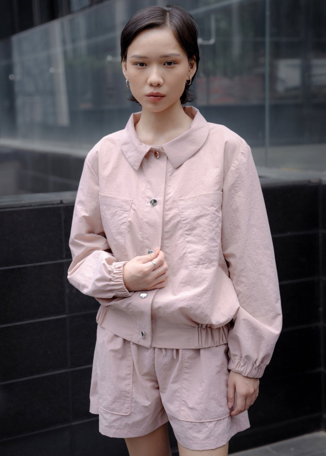 Person wearing a light pink outfit standing against a dark tiled wall.