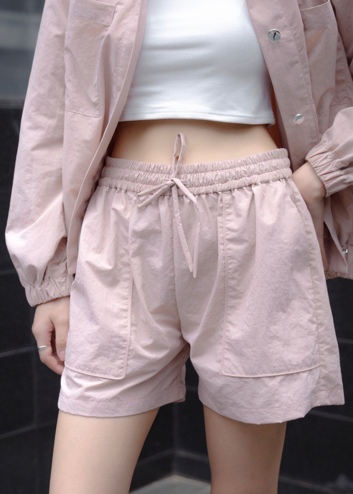 Person wearing light pink shorts and jacket with a white top against a dark background