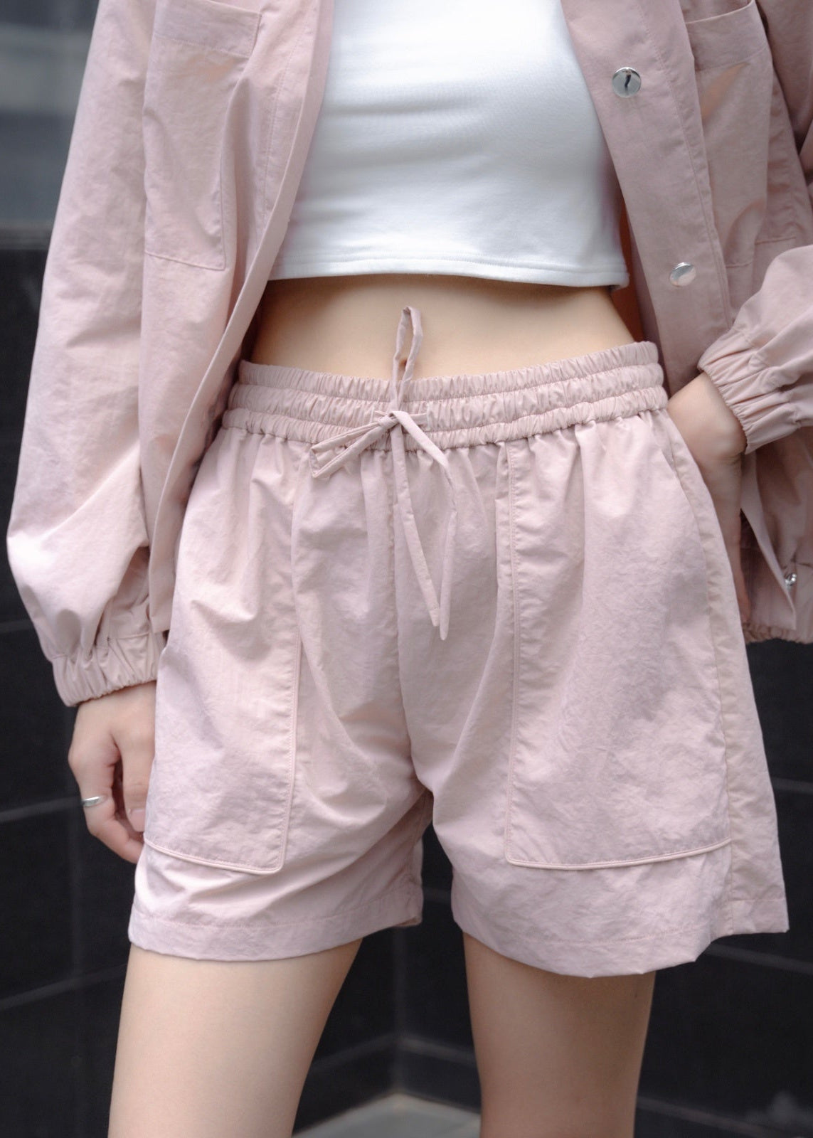 Person wearing light pink shorts and jacket with a white top against a dark background