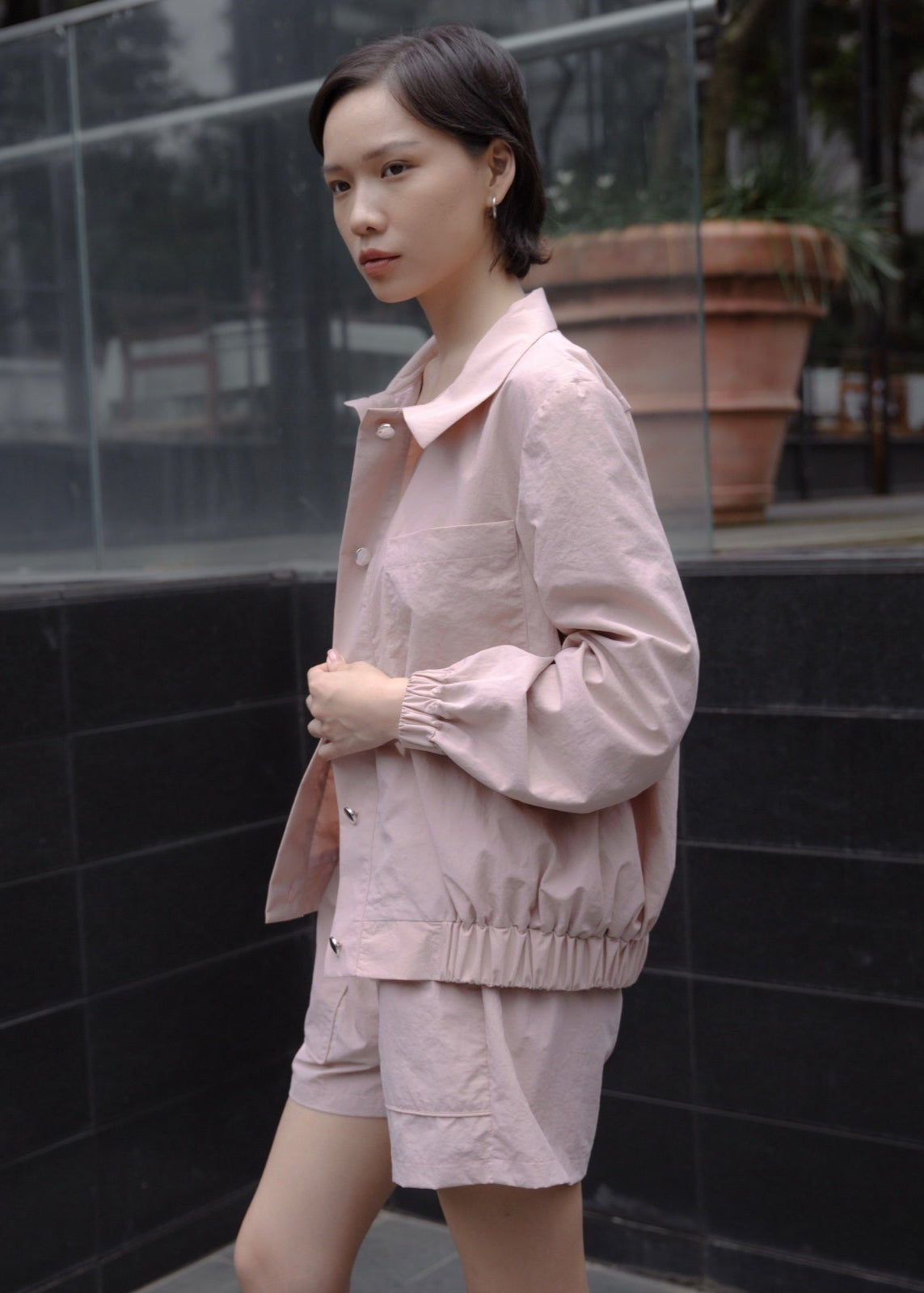 Woman wearing a pink outfit standing against a black tiled wall.