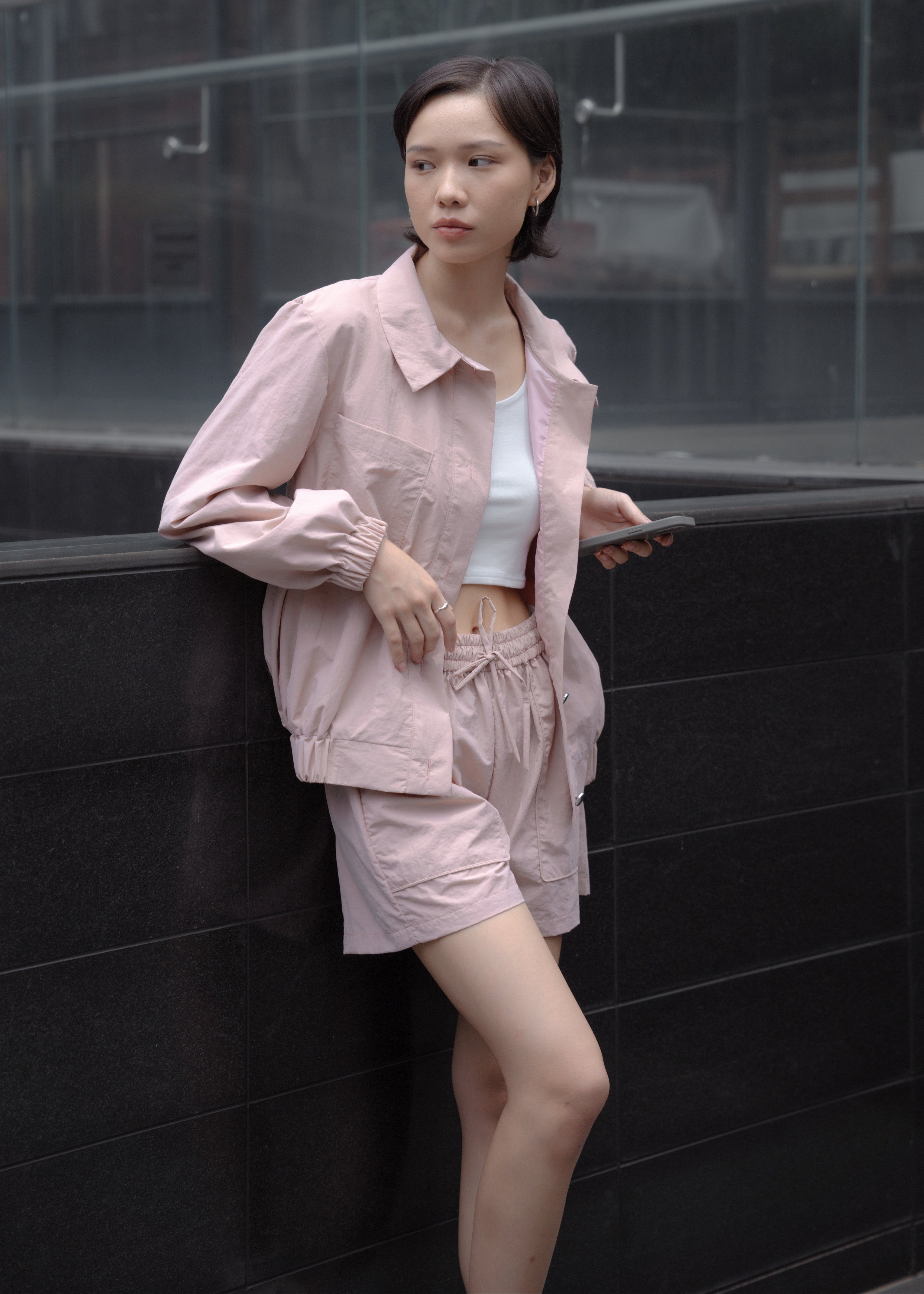 Woman in a pink outfit leaning against a black wall.