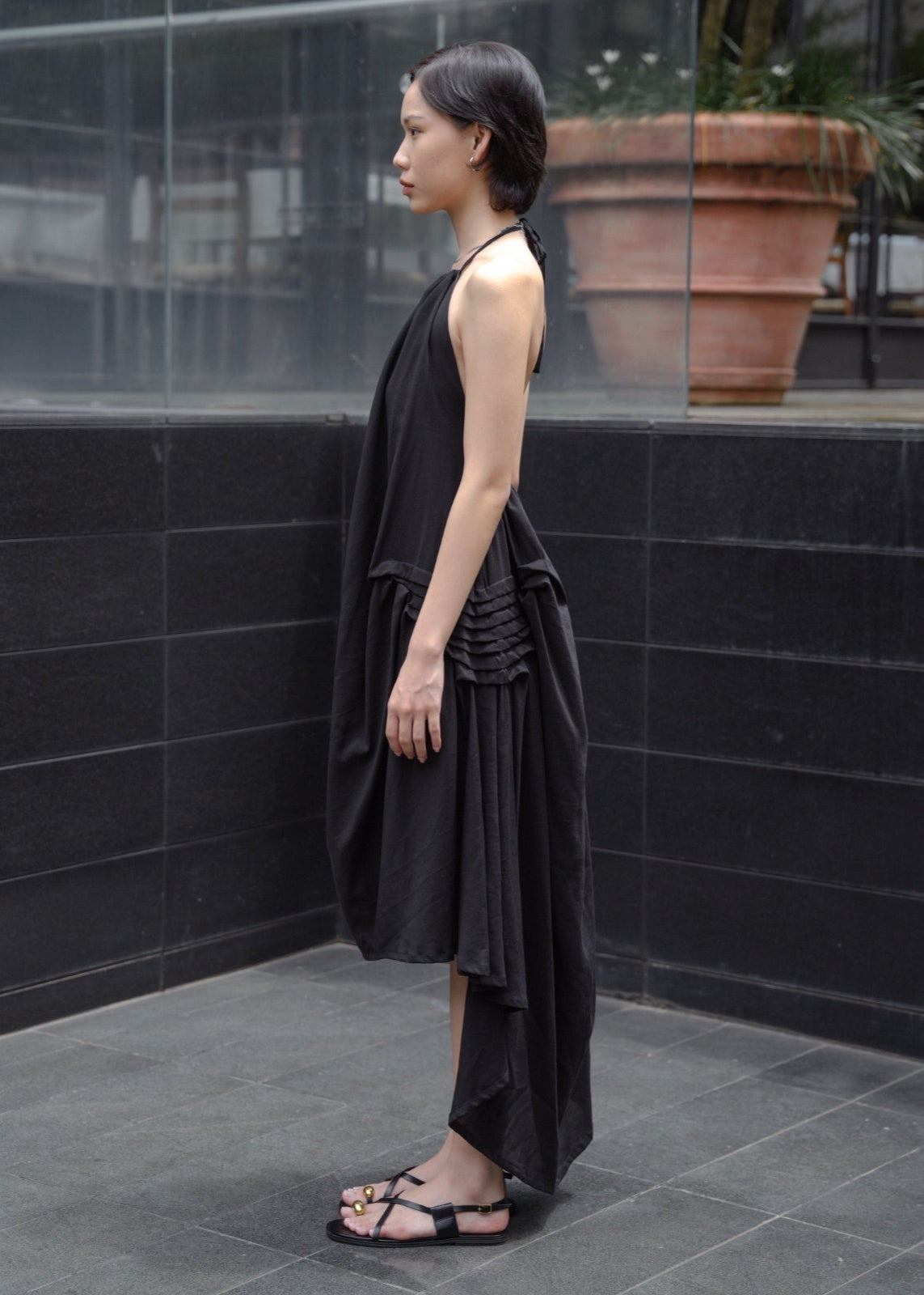 Woman wearing a black sleeveless dress standing against a black tiled wall.