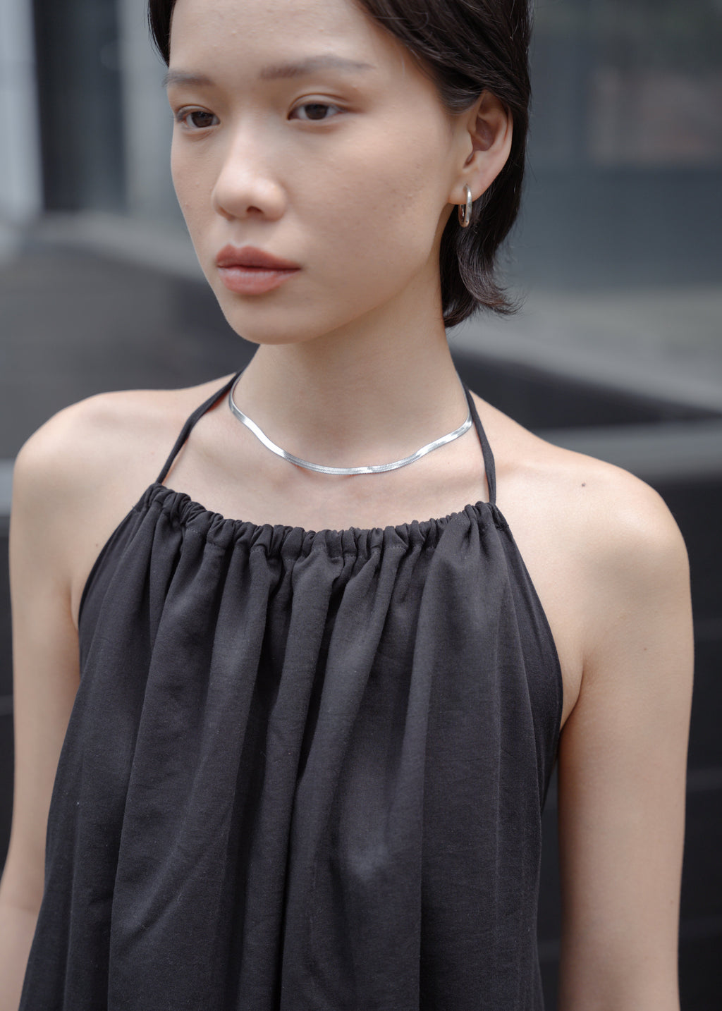 Woman wearing a black top and silver necklace against a blurred background