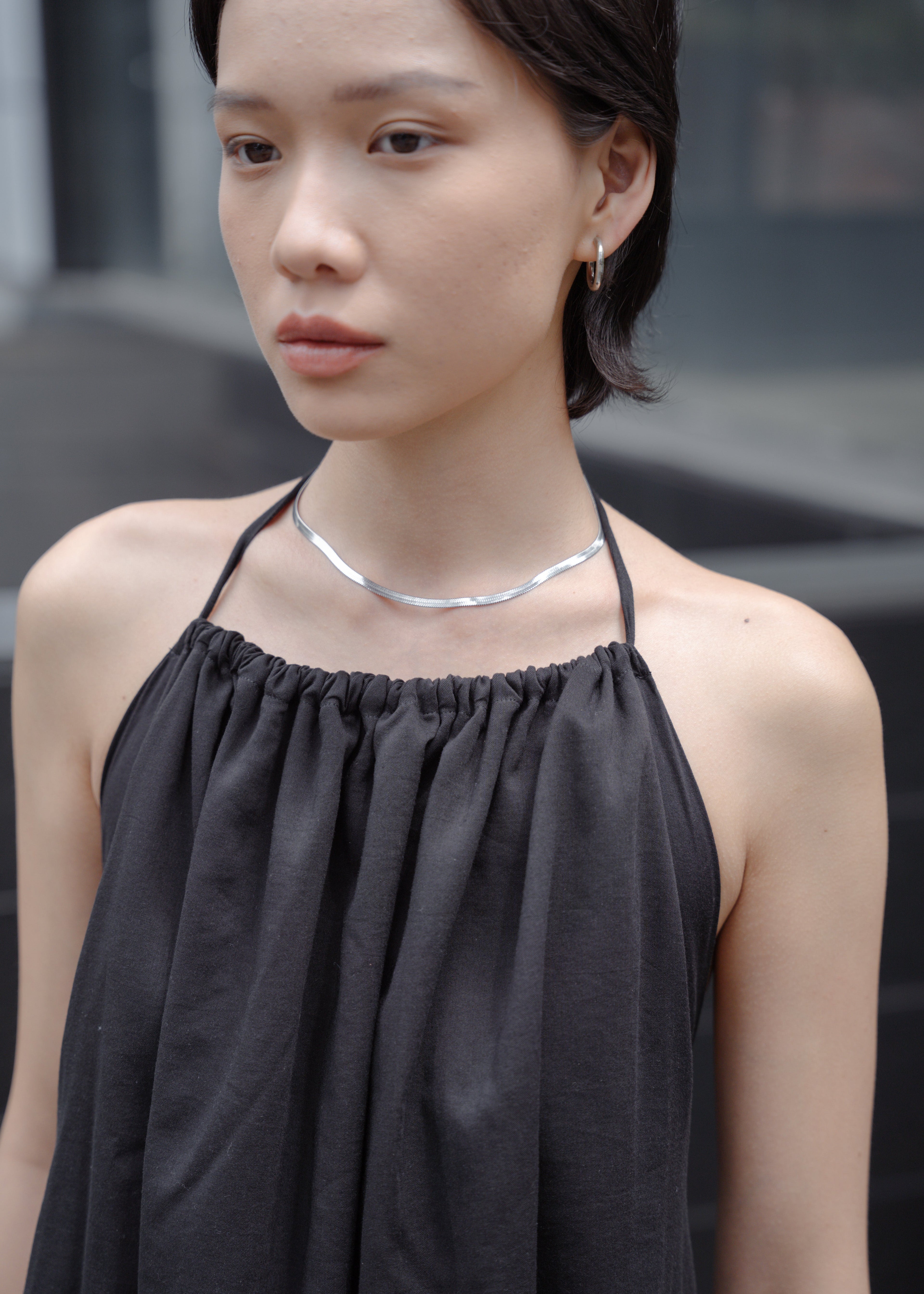 Woman wearing a black top and silver necklace against a blurred background