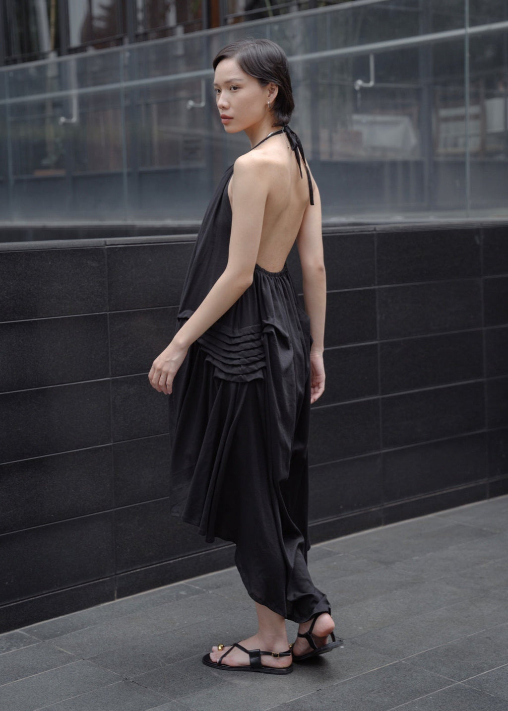 Woman wearing a black dress standing against a dark tiled wall.