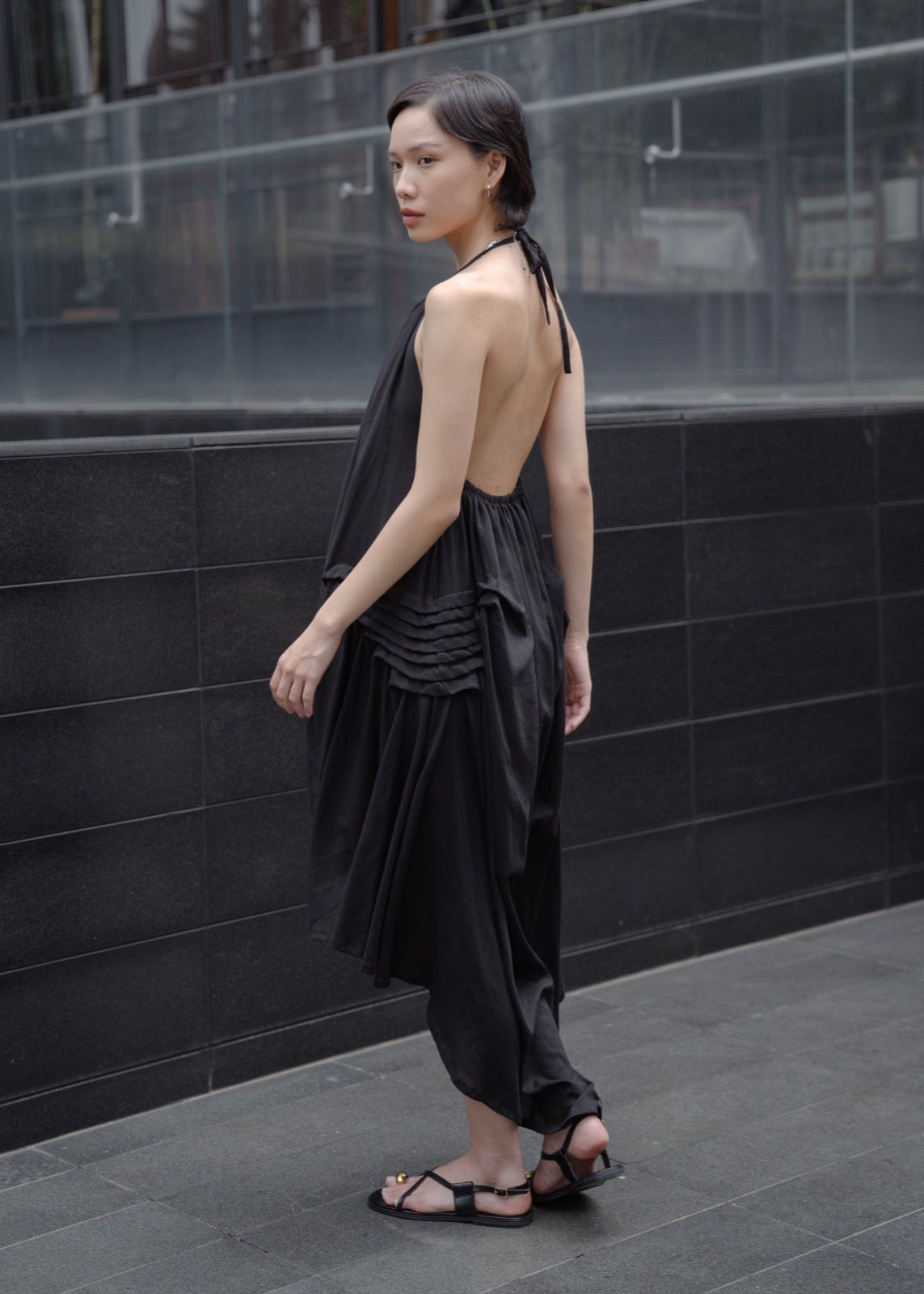 Woman wearing a black dress standing against a dark tiled wall.