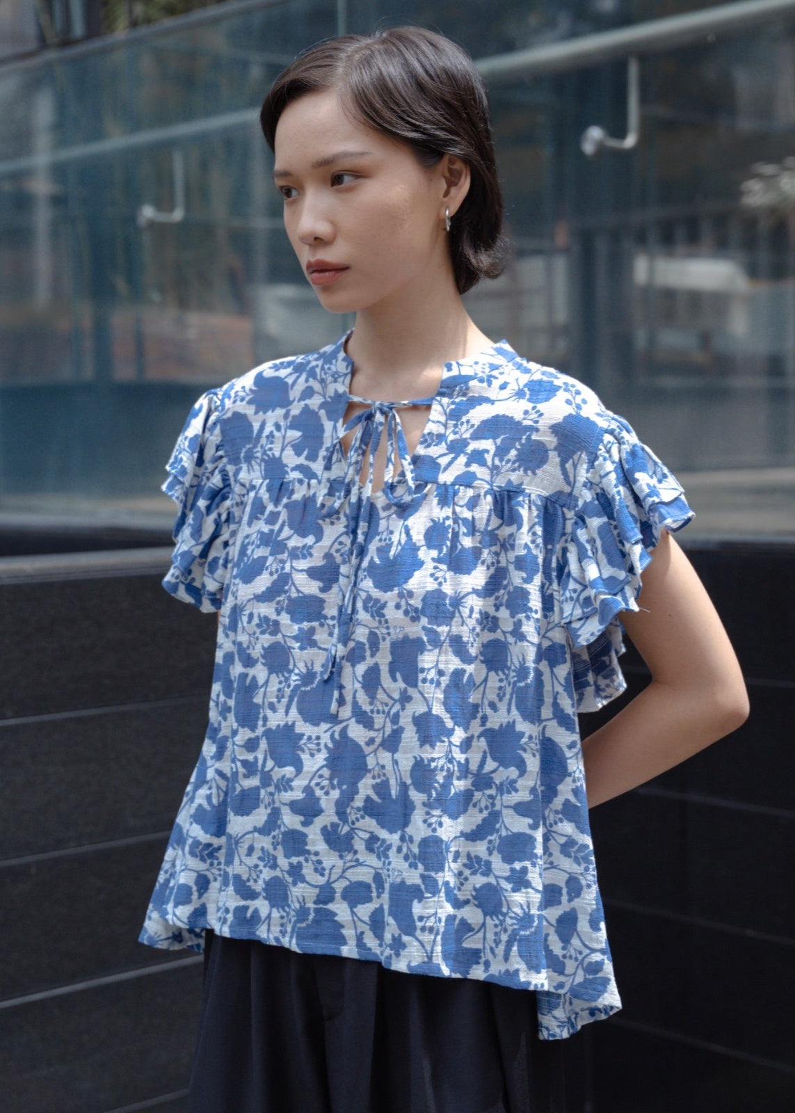 Woman wearing a blue floral blouse standing against a reflective glass wall.