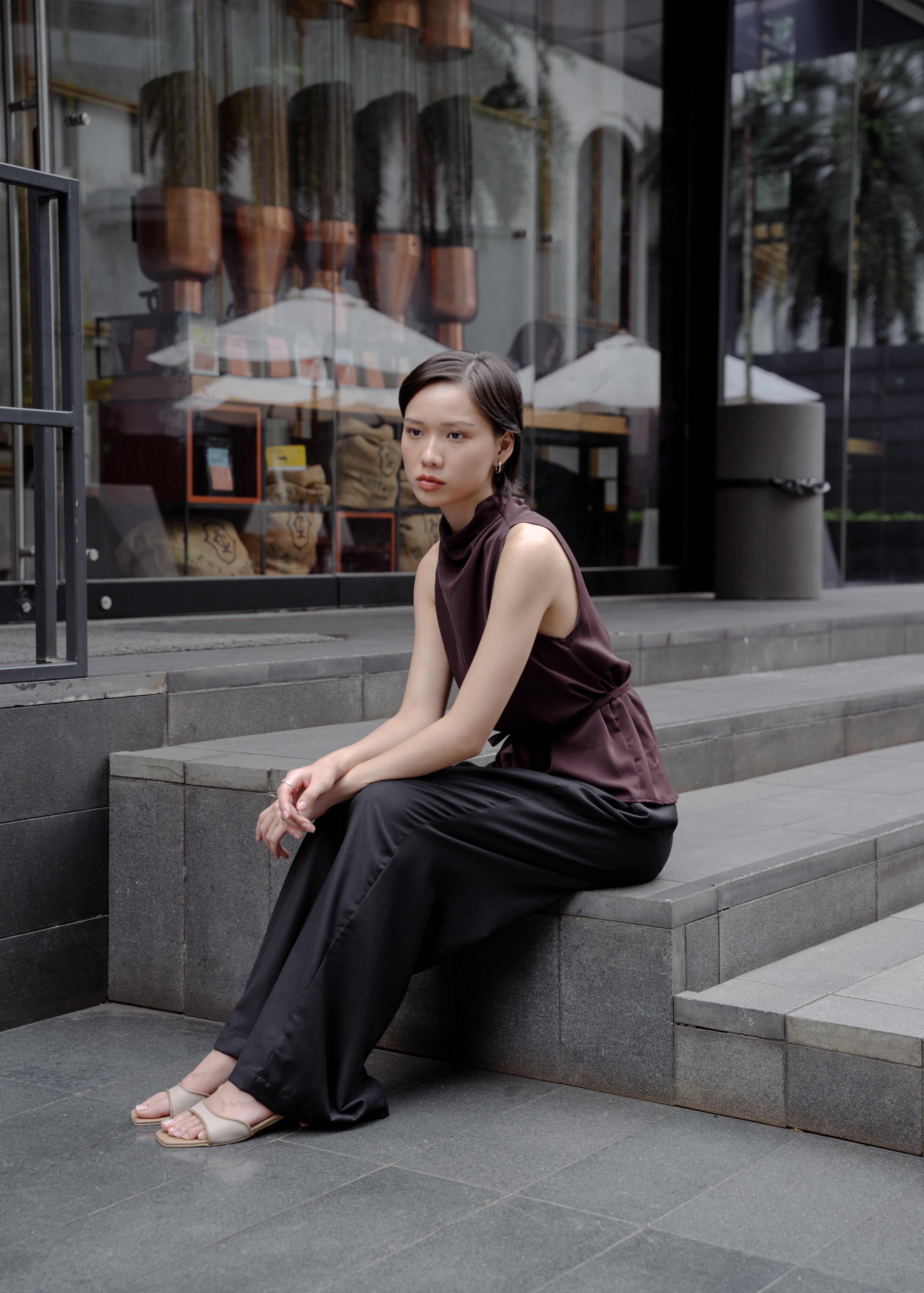 Woman sitting on steps in front of a store with reflective glass windows.