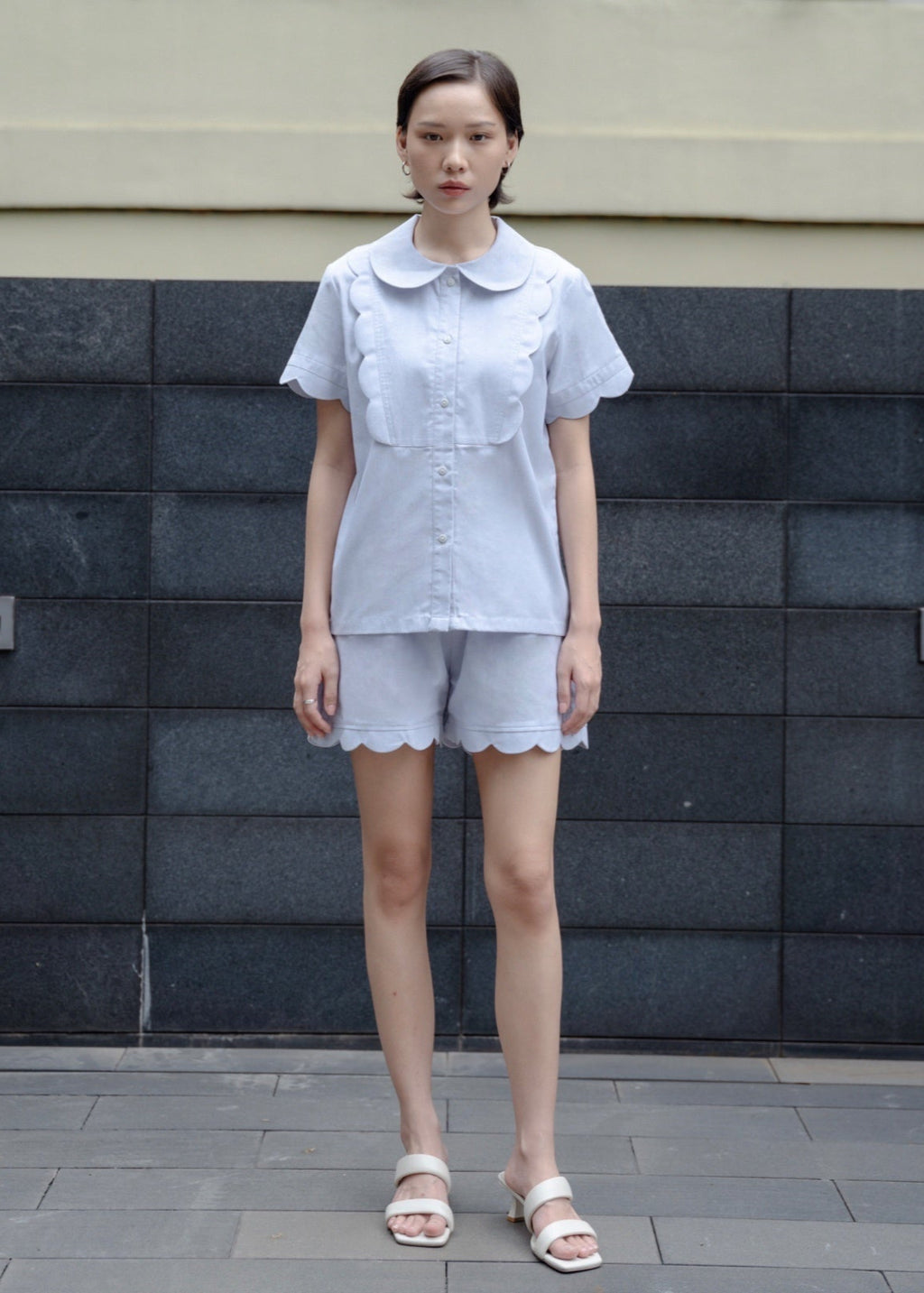 Woman wearing a light blue outfit standing against a textured wall.