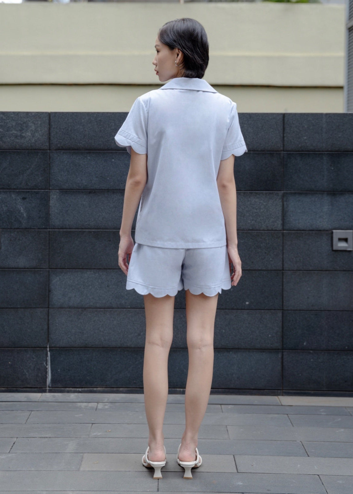 Woman wearing a light gray outfit standing against a textured wall.