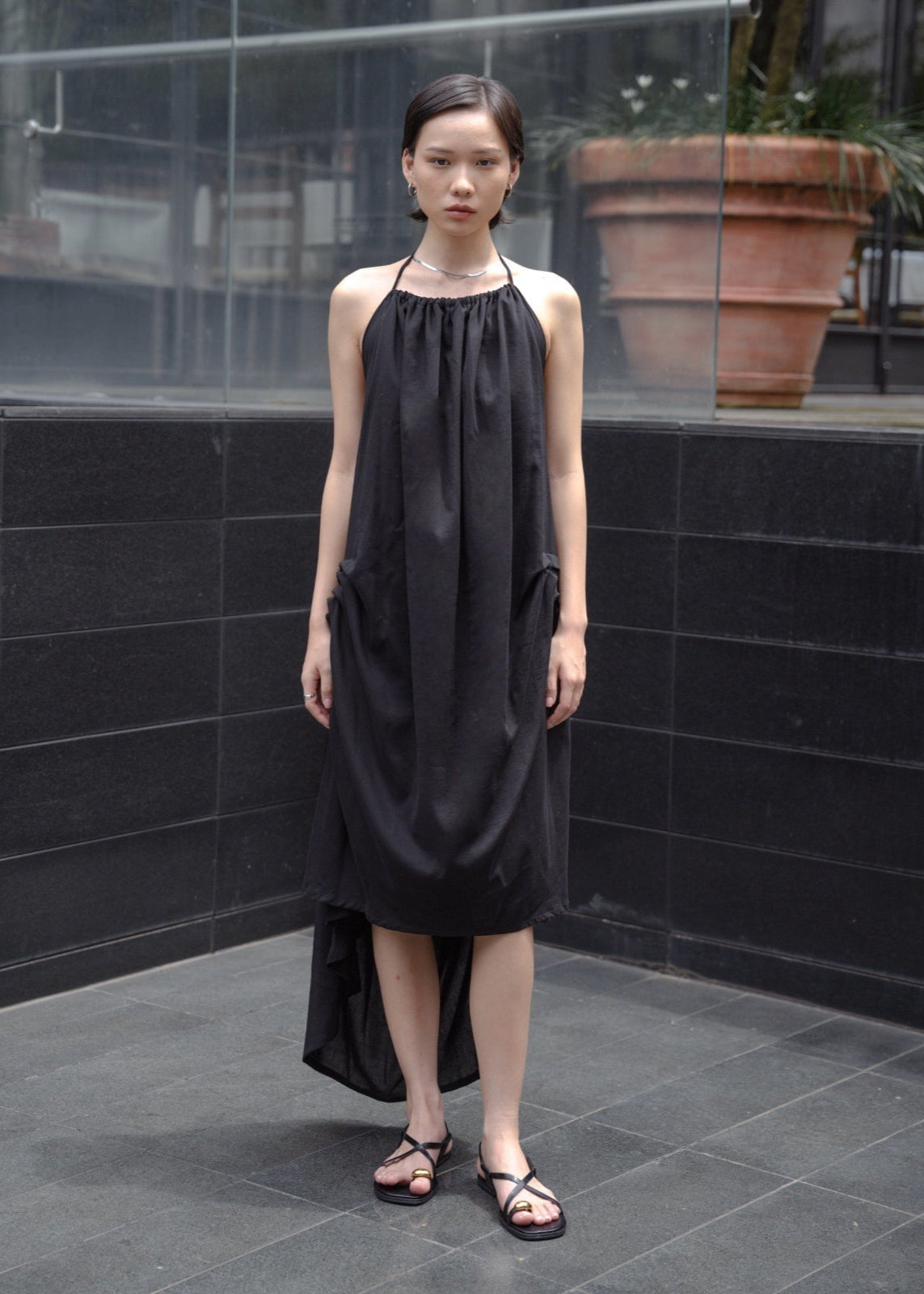 Woman wearing a black sleeveless dress standing against a black tiled wall.