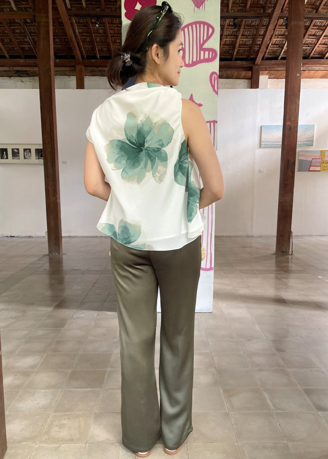 Woman wearing a sleeveless top with a floral design and green pants in an indoor setting.