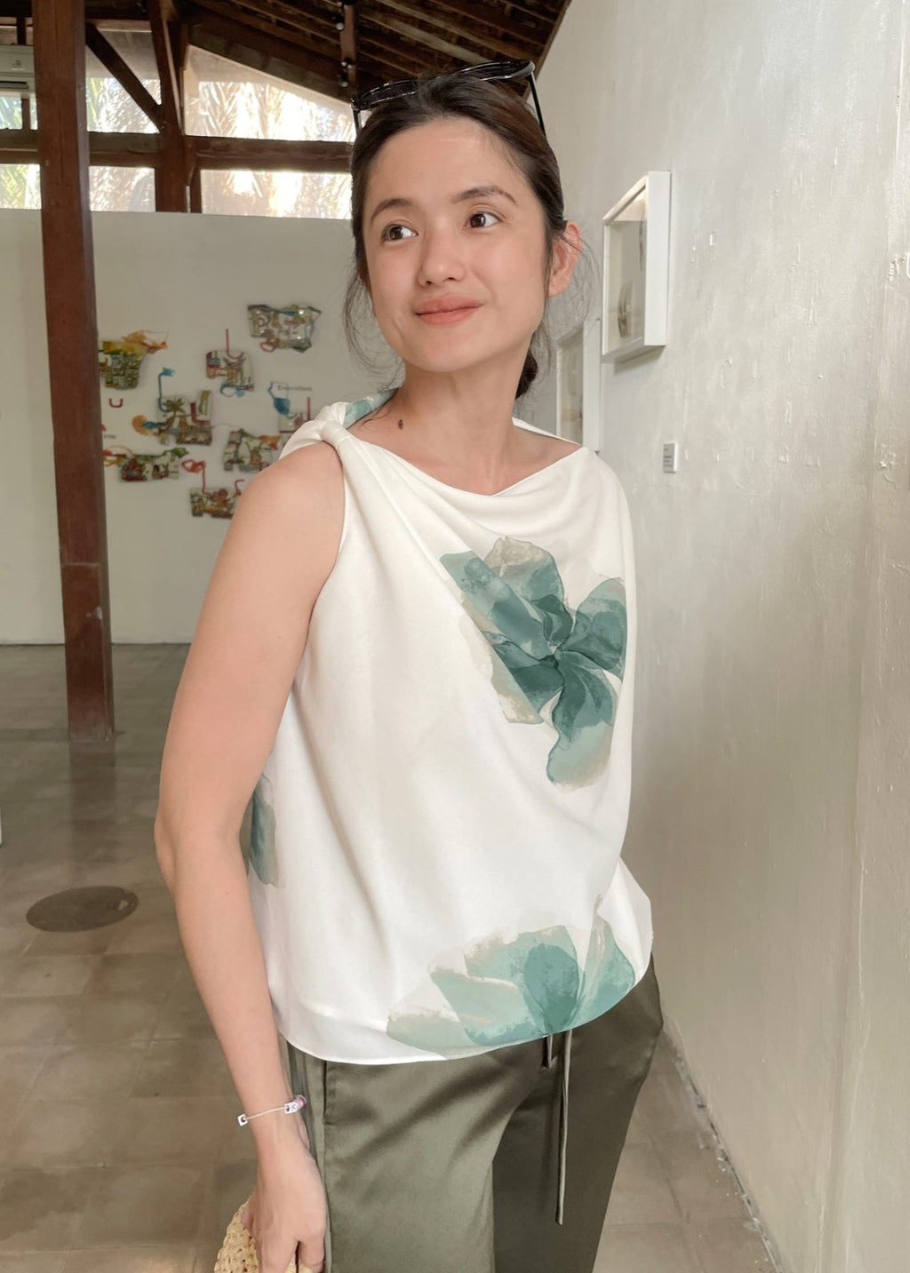 Woman wearing a white sleeveless top with green floral patterns in an indoor setting.