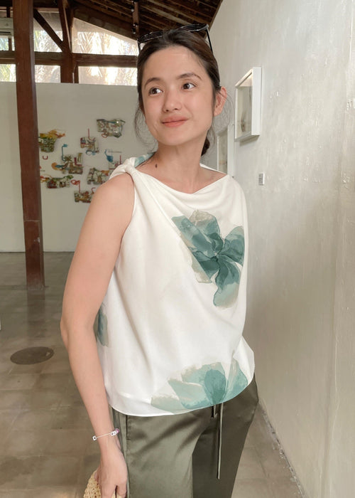 Woman wearing a white sleeveless top with green floral patterns in an indoor setting.