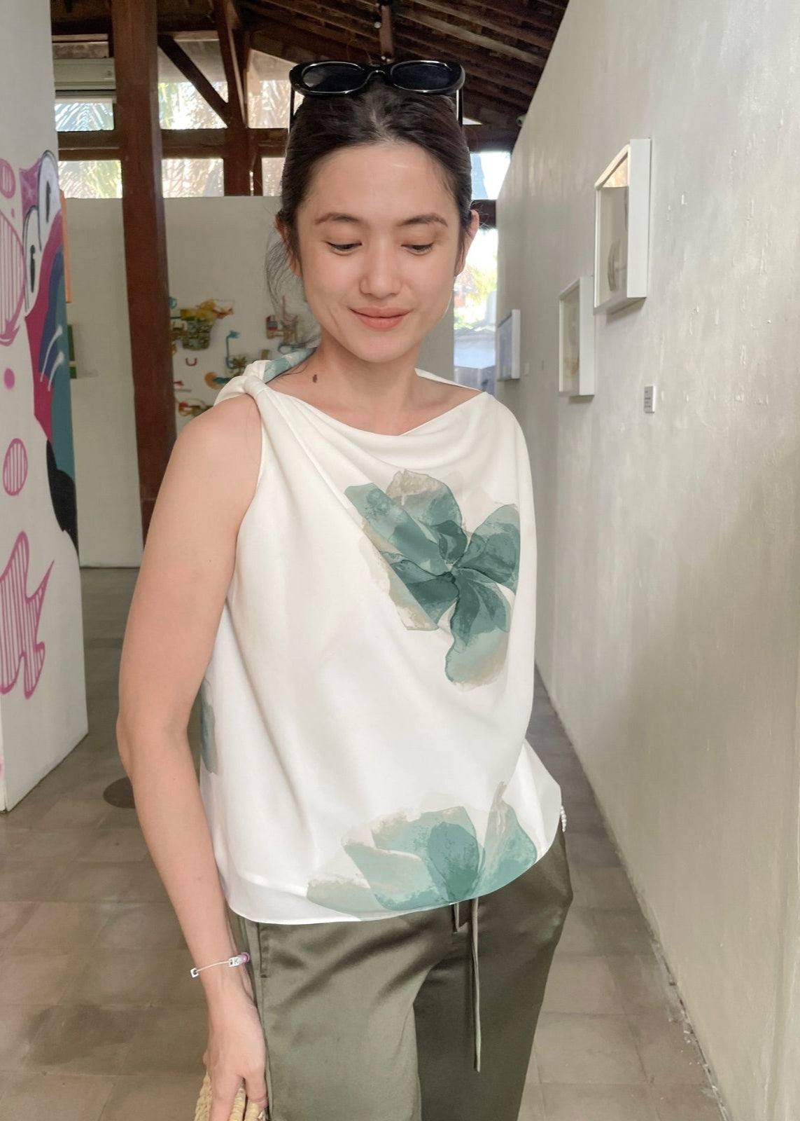 Woman wearing a white sleeveless top with green floral designs in an indoor setting.