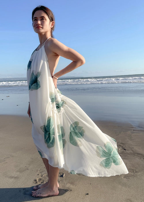 Woman in a floral dress standing on a beach with ocean waves in the background