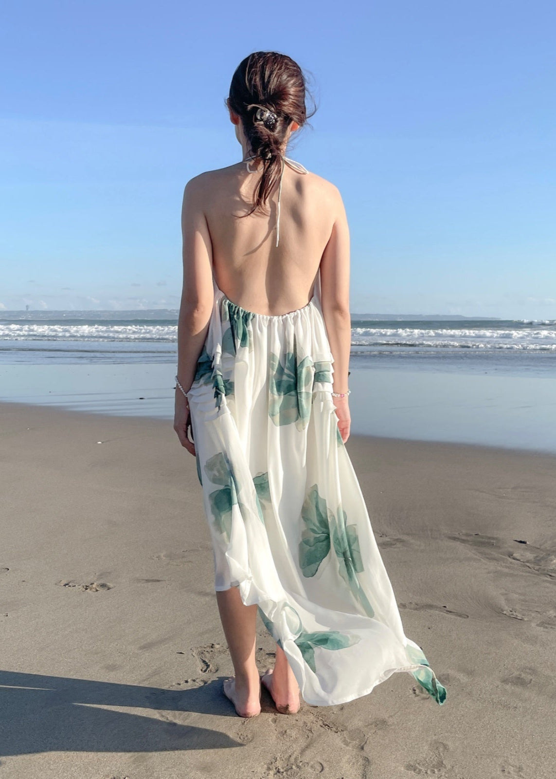 Woman in a floral dress standing on a beach with ocean view