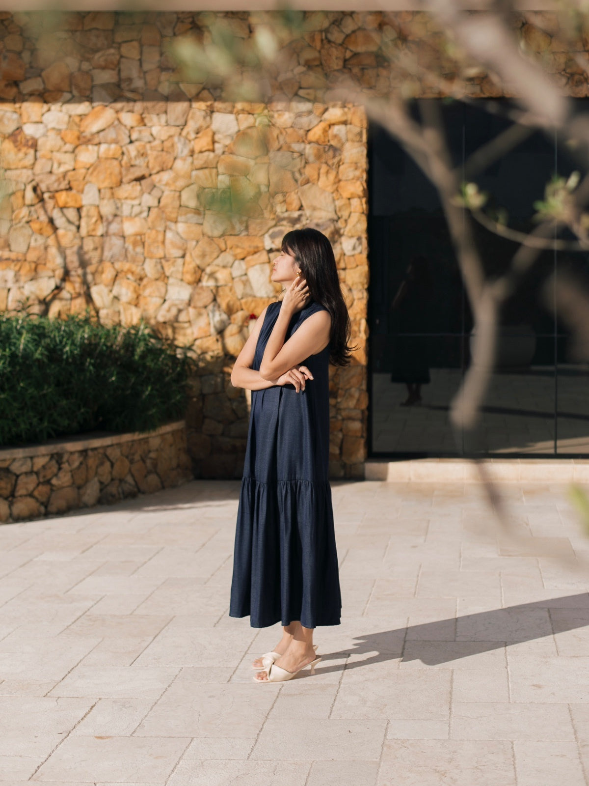 Woman in a navy dress standing outdoors near a stone wall.