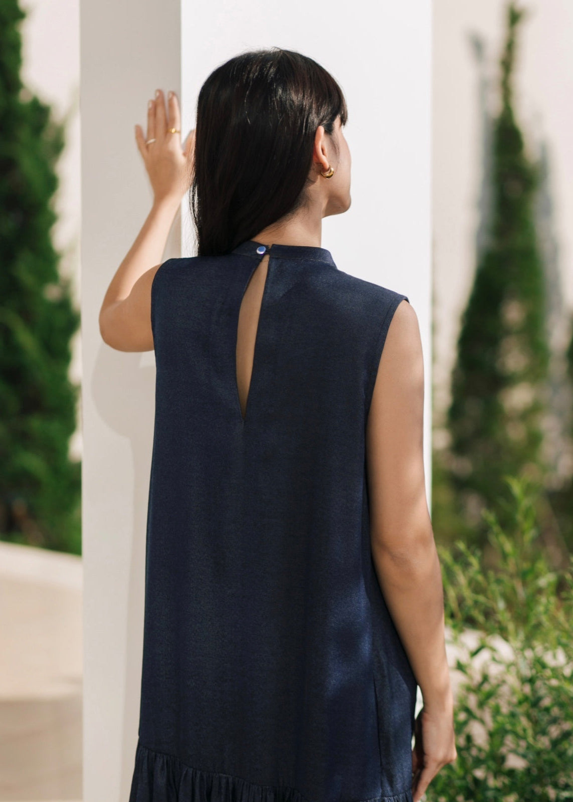 Woman wearing a navy sleeveless dress with a cutout back, standing outdoors.