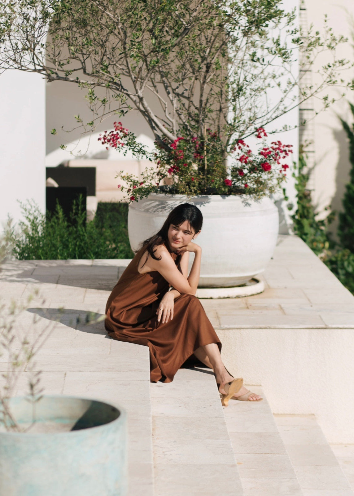 Woman in a brown dress sitting outdoors with plants and flowers in the background