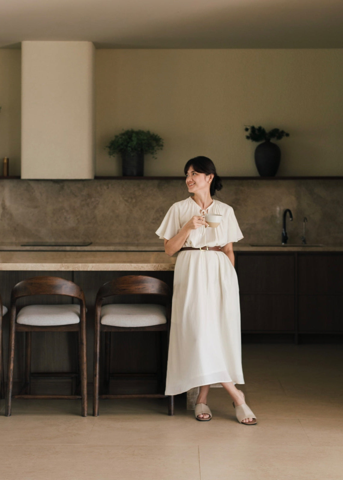 Woman in a white dress standing in a modern kitchen.