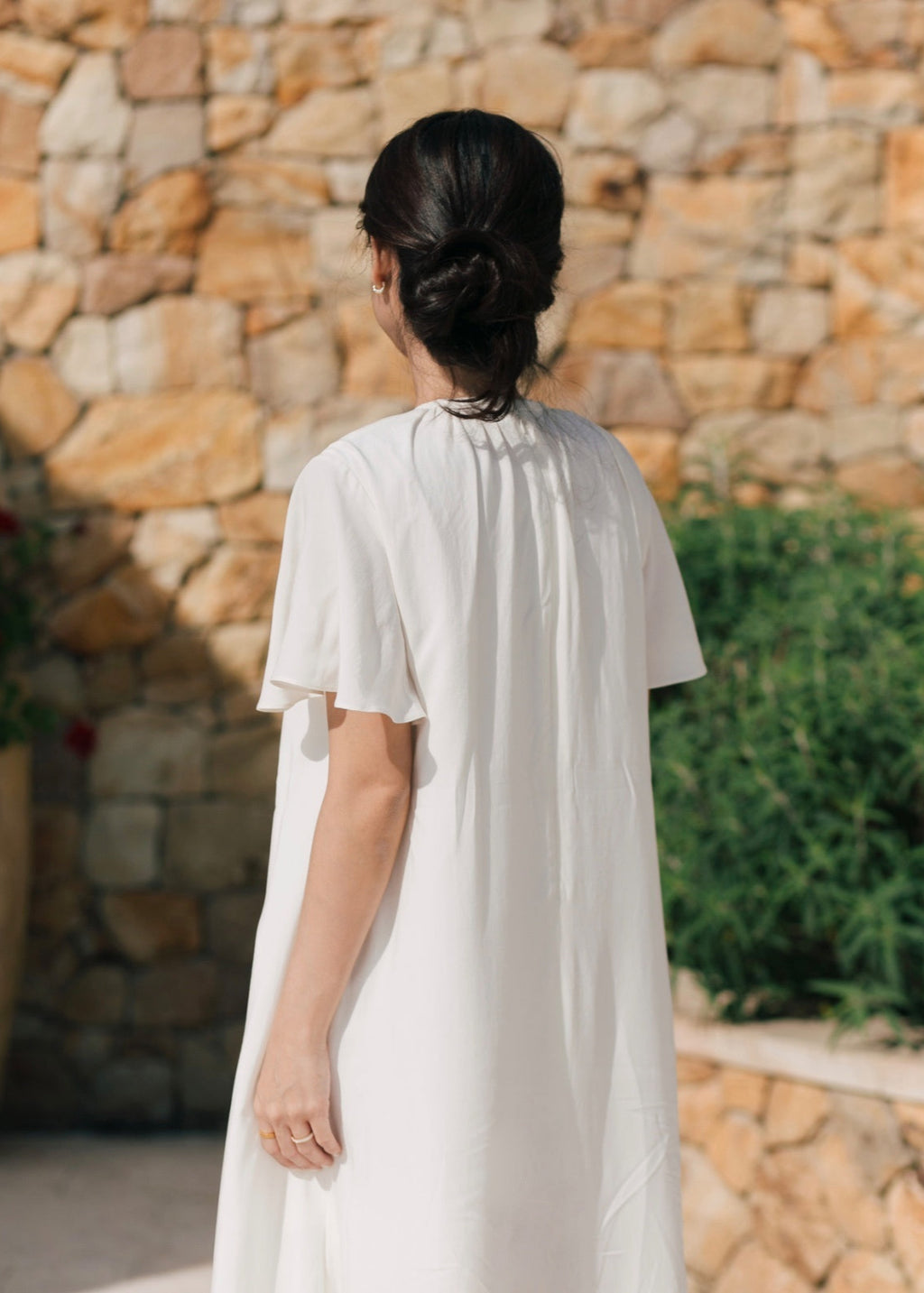 Person wearing a white dress standing in front of a stone wall.