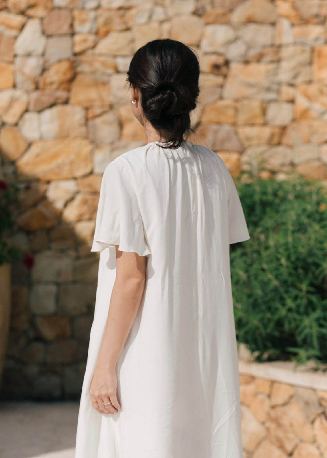 Person wearing a white dress standing in front of a stone wall.