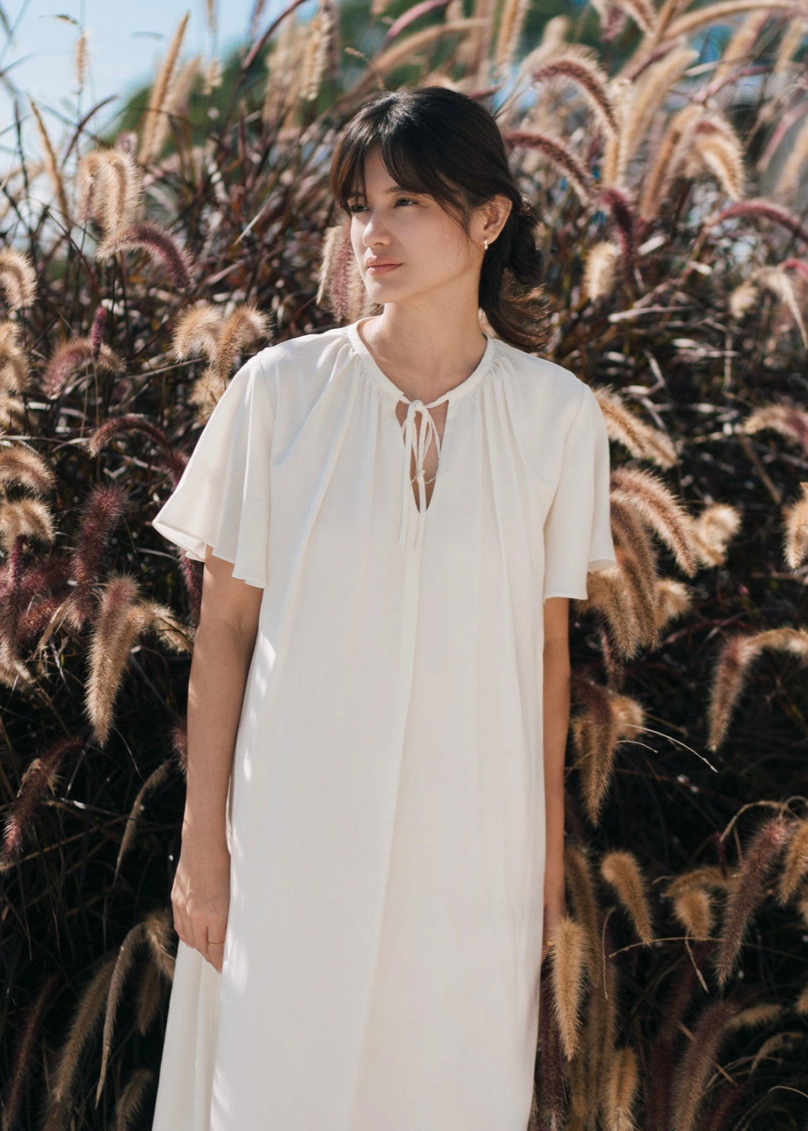 Woman in a white dress standing in front of tall grasses