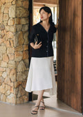 Woman in black jacket and white skirt standing in a modern interior setting with stone and wooden elements.
