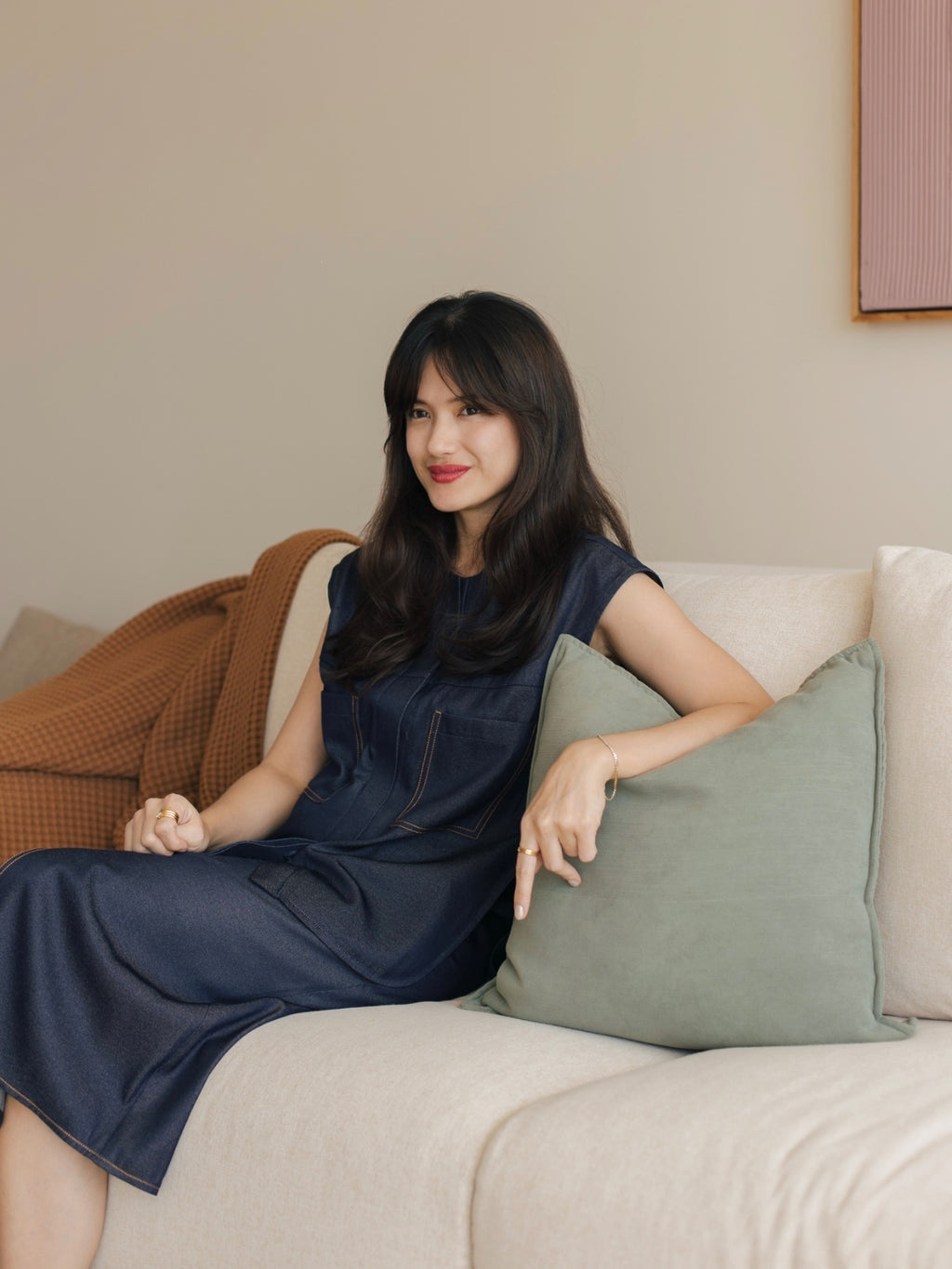 Woman in a blue dress sitting on a beige couch with a neutral background