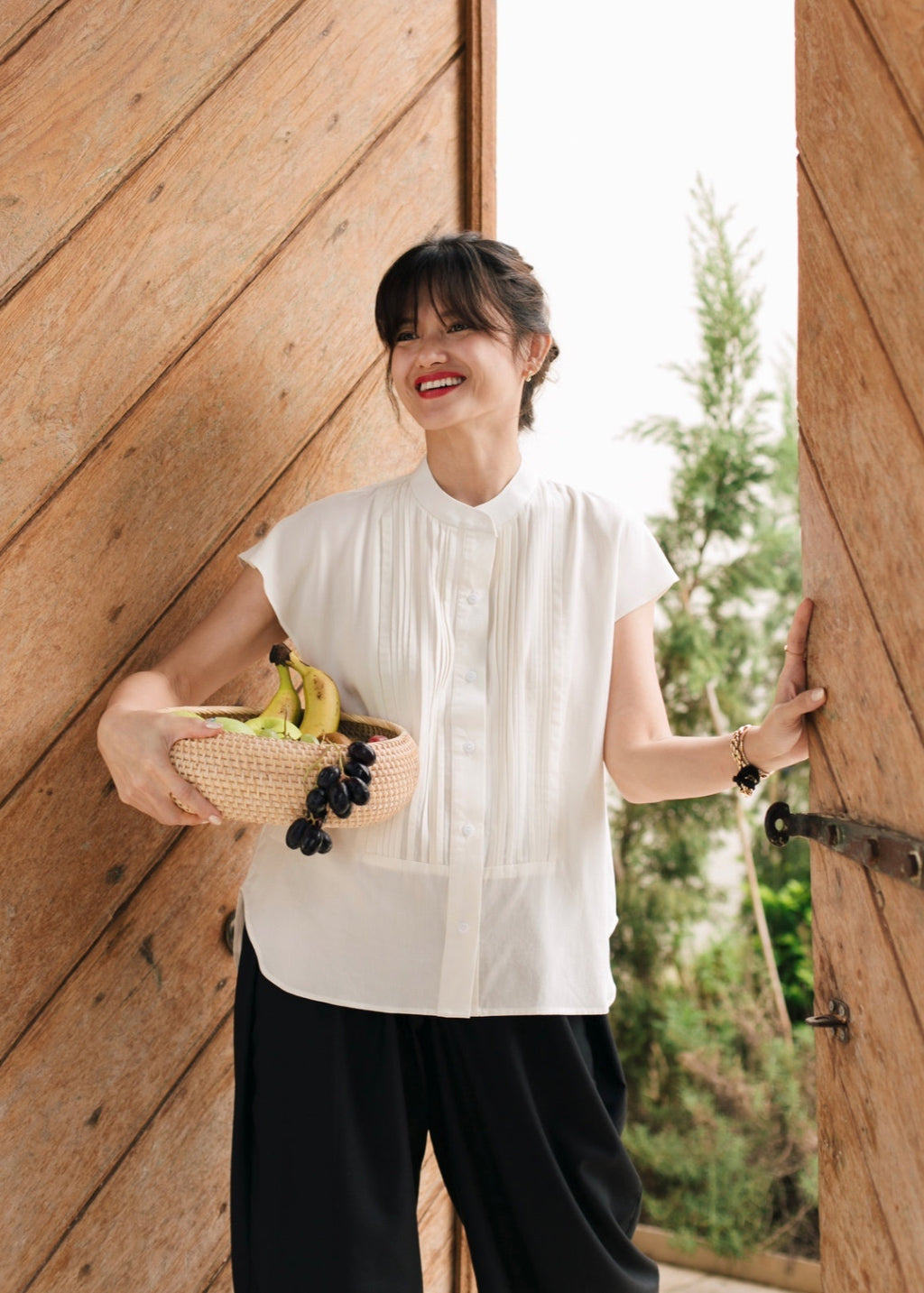 Woman holding a basket with fruits and vegetables against a wooden wall.