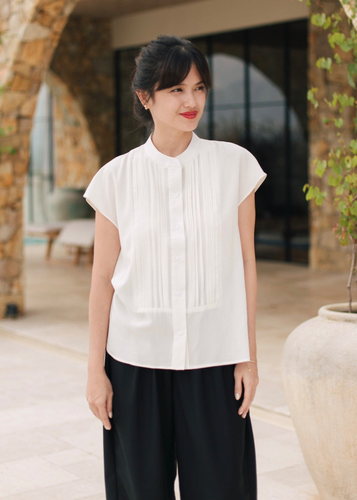Woman wearing a white blouse and black pants standing outdoors.