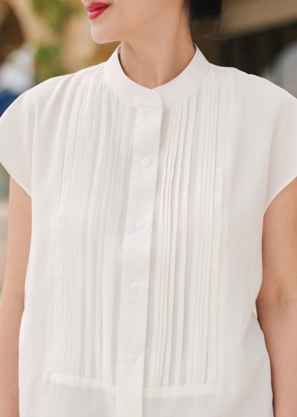 Close-up of a person wearing a white pleated blouse with blurred background